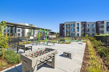 a playground with a fire pit and benches in front of an apartment building